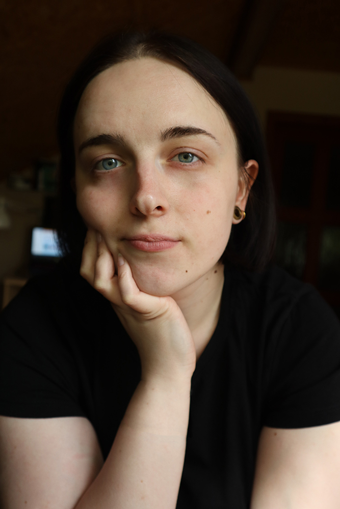 Na niewyraźnym tle jakiegoś wnętrza fotografia młodej dziewczyny. Jest nią zielonooka szatynka o gładko przedzielonych na środku włosach do ramion. Chcąc je odgarnąć z twarzy, odkryła ucho i ciemny kolczyk.\nSwą twarz zbliżyła do obiektywu i kładąc łokieć na jakimś blacie, policzek wsparła mocno na palcach prawej dłoni. Patrzy nam prosto w oczy i wygląda na zamyśloną. Ma na sobie czarną bluzkę z krótkim rękawem.\n