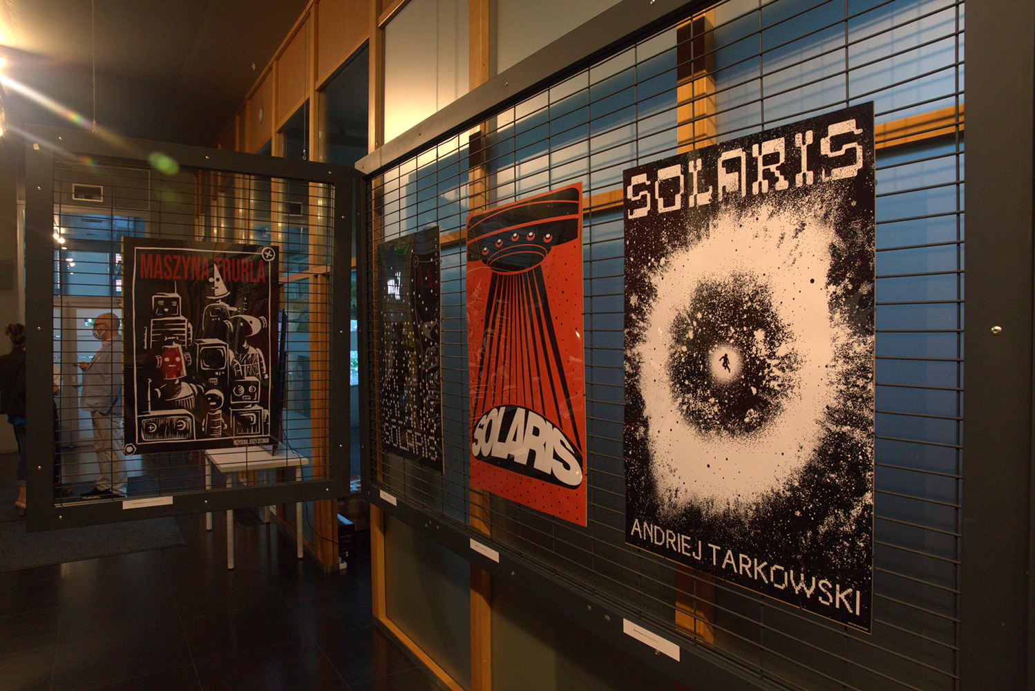 Kilka plakatów SOLARIS ujęto z głębi wnętrza galerii. Pomarańczowa ściana doświetlana dziennym światłem, teraz pod wpływem panującego na zewnątrz mroku jest granatowa