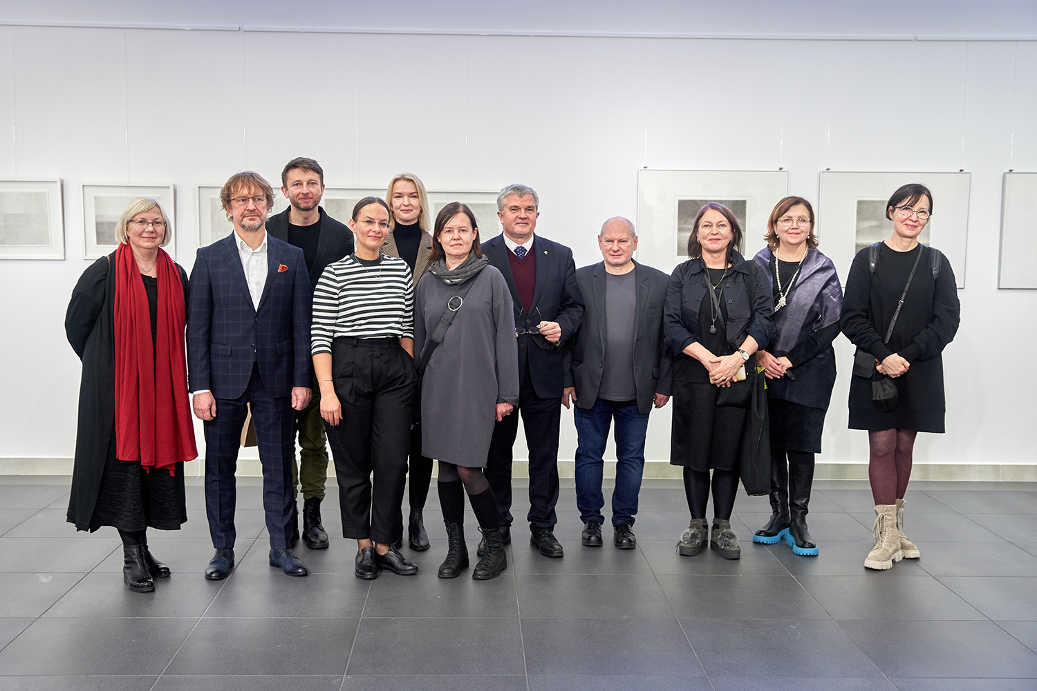 Na tle jasnych ścian galerii Hol eksponującej grafikę, stoi jedenaście osób, wśród których znajdują się między innymi wykładowcy i artyści, oraz Rektor ASP w Łodzi.